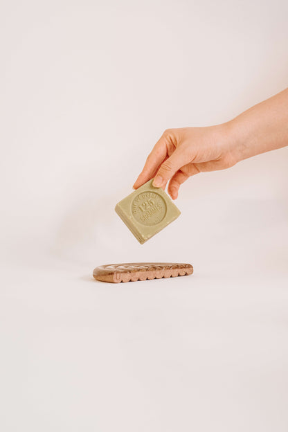 Hand holding a bar of soap above a soap dish on a plain background